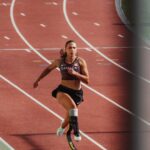 Canadian Paralympic sprinter Marissa Papaconstantinou running on track with blade prosthetic in national team gear
