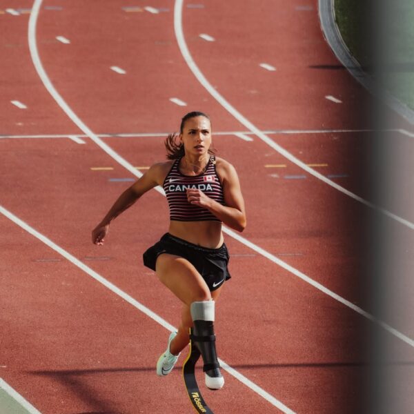 Canadian Paralympic sprinter Marissa Papaconstantinou running on track with blade prosthetic in national team gear