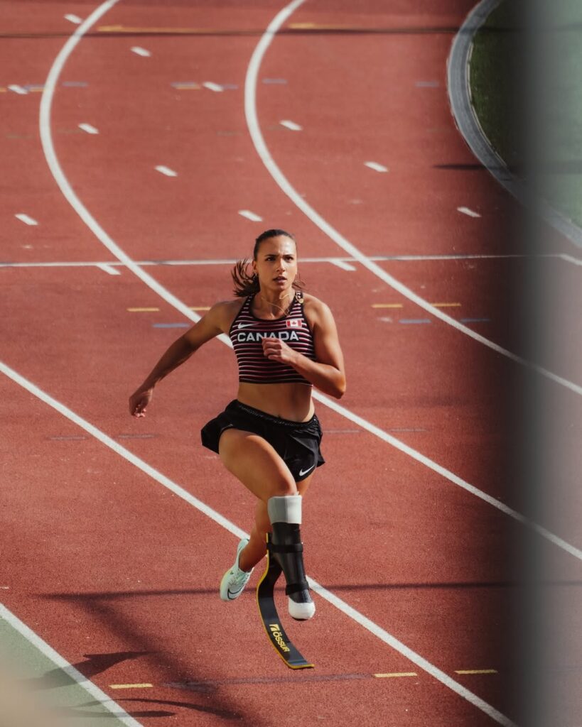 Canadian Paralympic sprinter Marissa Papaconstantinou running on track with blade prosthetic in national team gear