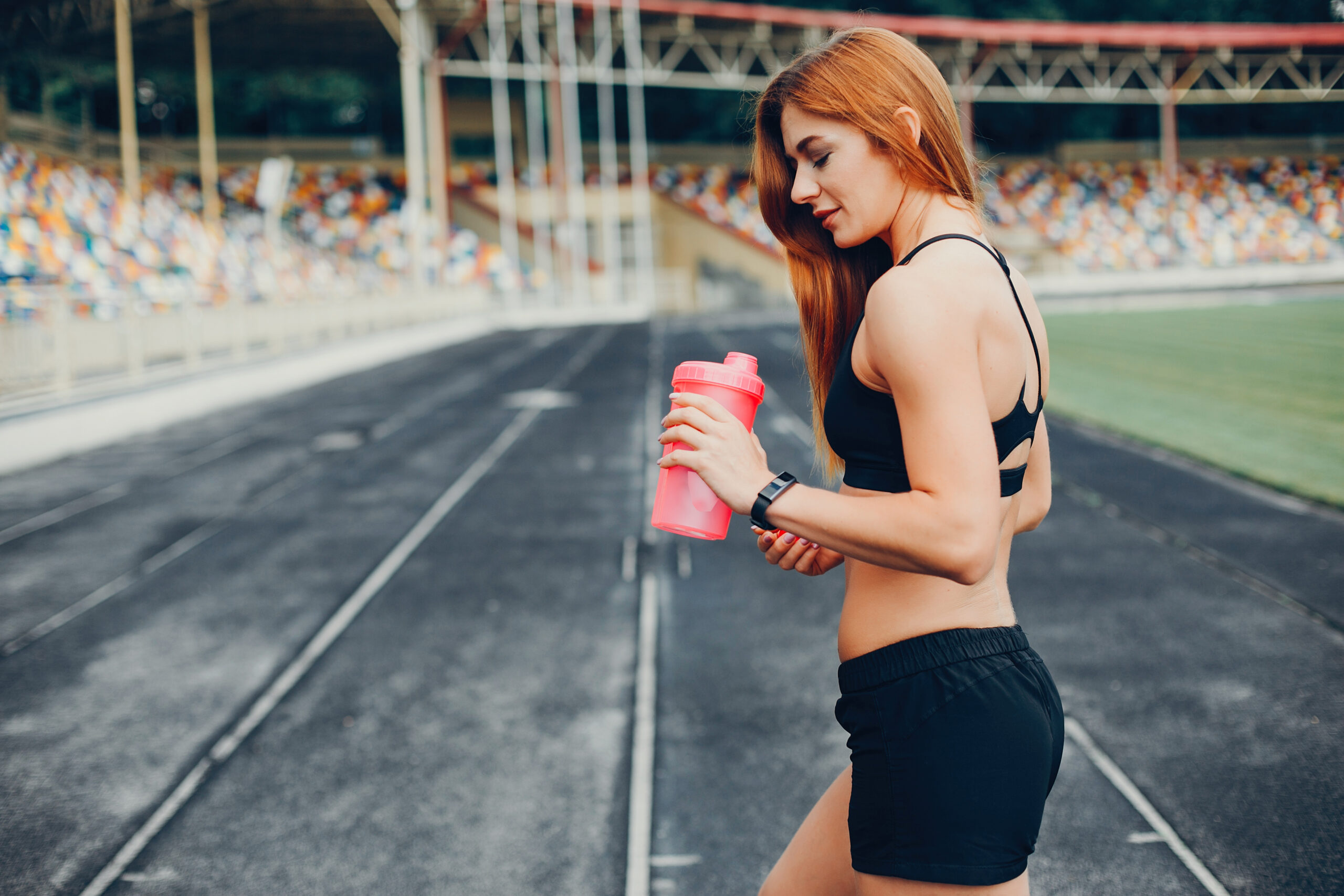 A lady in fitness clothes, in track and holding a bottle
